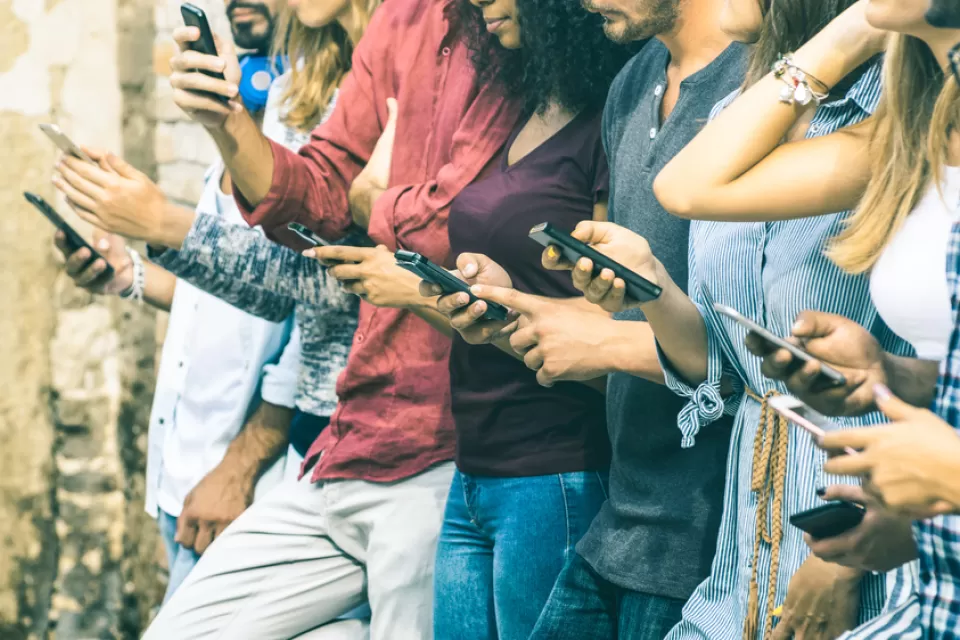 A row of young people outdoors using smartphones